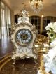Horloge de table en céramique fine, décorée de détails dorés, fabriquée à la main avec un soin artisanal.